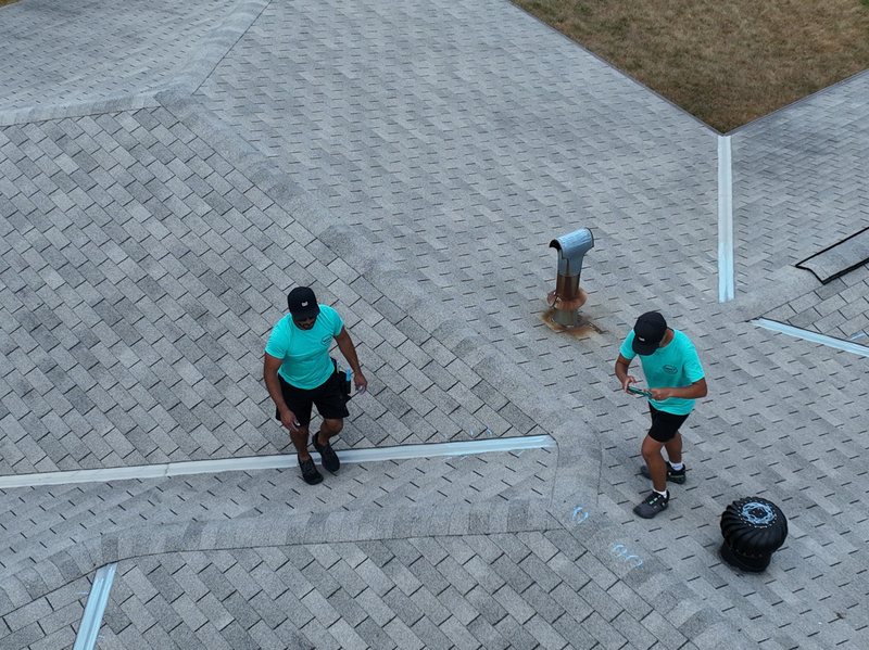 Two Mint Exteriors crew in teal shirts walking the old roof, chalk marks on the shingles around a vent
